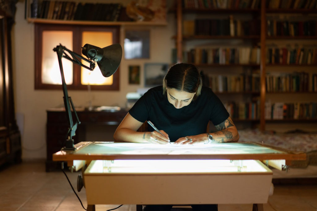 Tattooed woman sketching on a light table in a studio